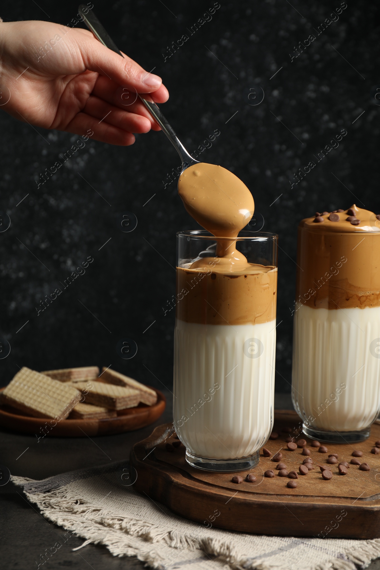 Photo of Woman pouring cream for dalgona coffee into glass at dark table, closeup