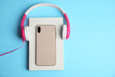 Photo of Book, modern headphones and smartphone on light blue background, top view. Space for text