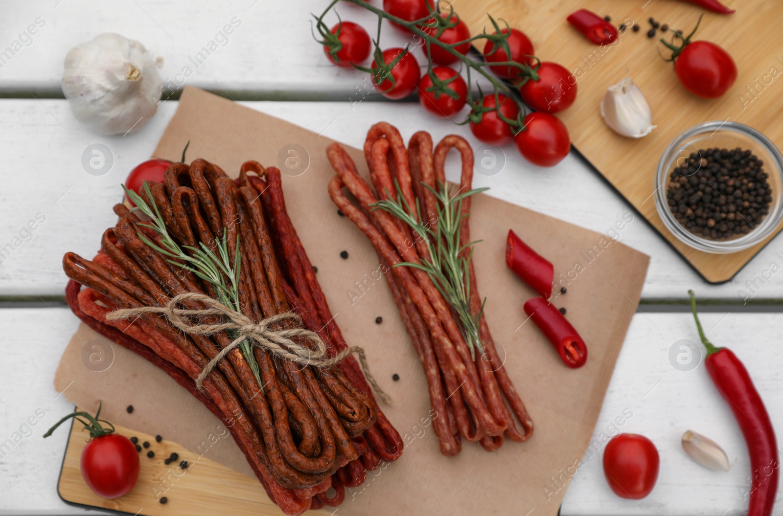 Photo of Delicious kabanosy with rosemary, peppercorn, chilli and tomatoes on white wooden table, flat lay