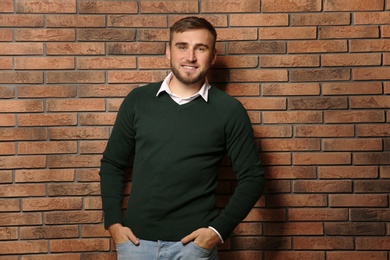 Photo of Handsome young man in warm sweater near brick wall