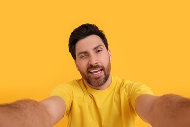 Smiling man taking selfie and winking on yellow background
