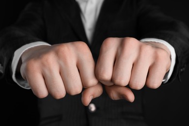 Photo of Businessman showing fists with space for tattoo on black background, closeup