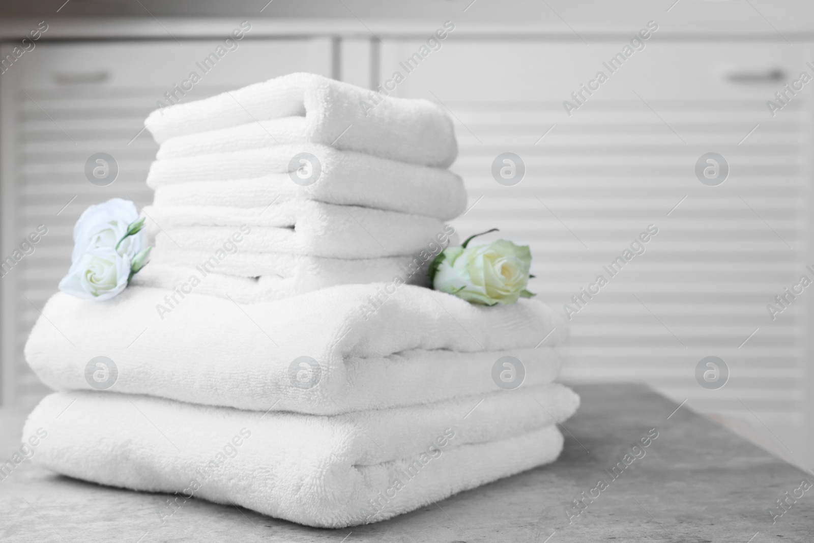 Photo of Folded towels with flowers on grey table indoors