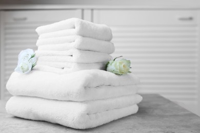 Photo of Folded towels with flowers on grey table indoors