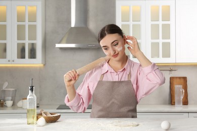 Photo of Thoughtful woman with soiled face holding rolling pin at messy table in kitchen