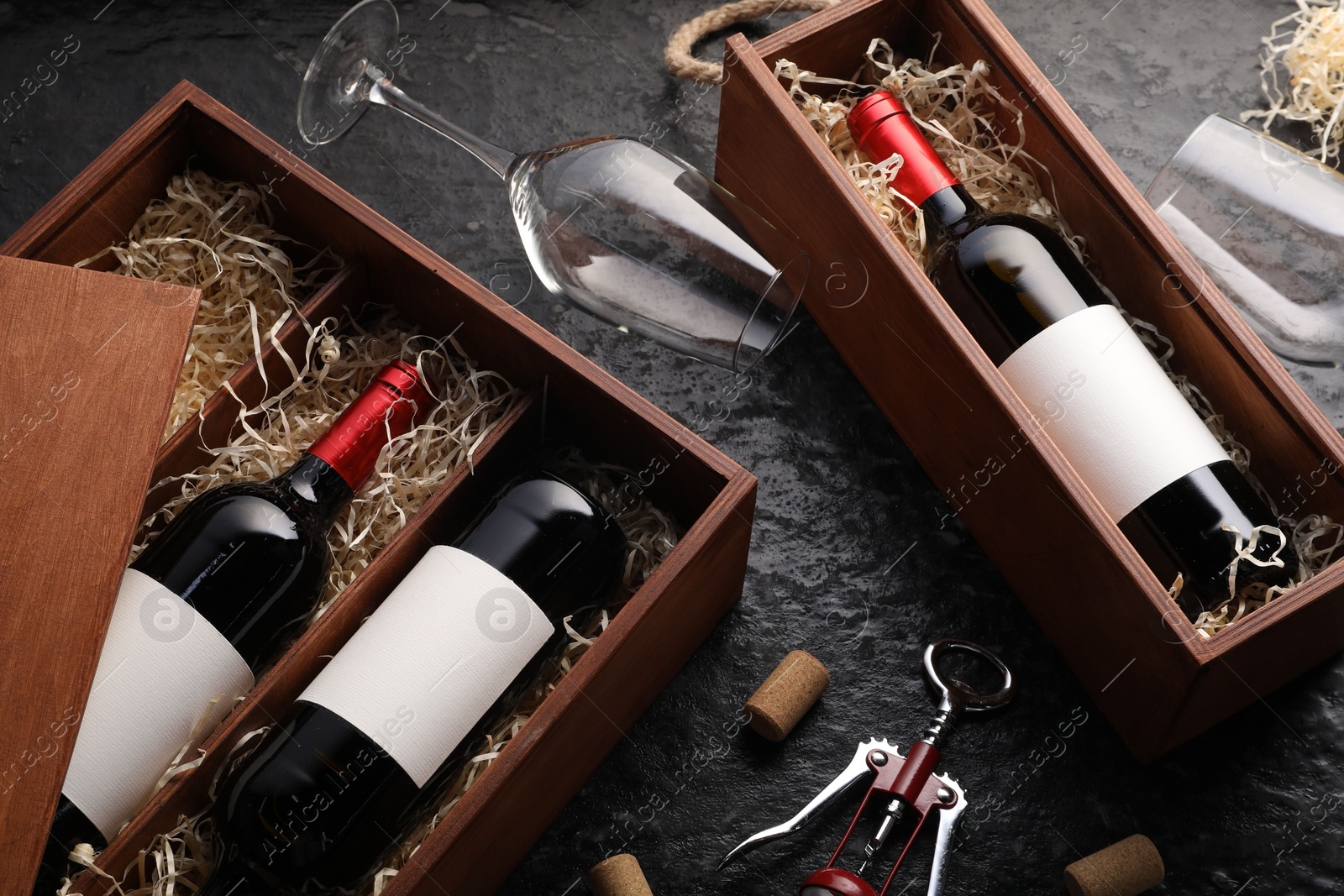 Photo of Bottles of wine in wooden boxes, glasses, corkscrew and corks on dark textured table, above view