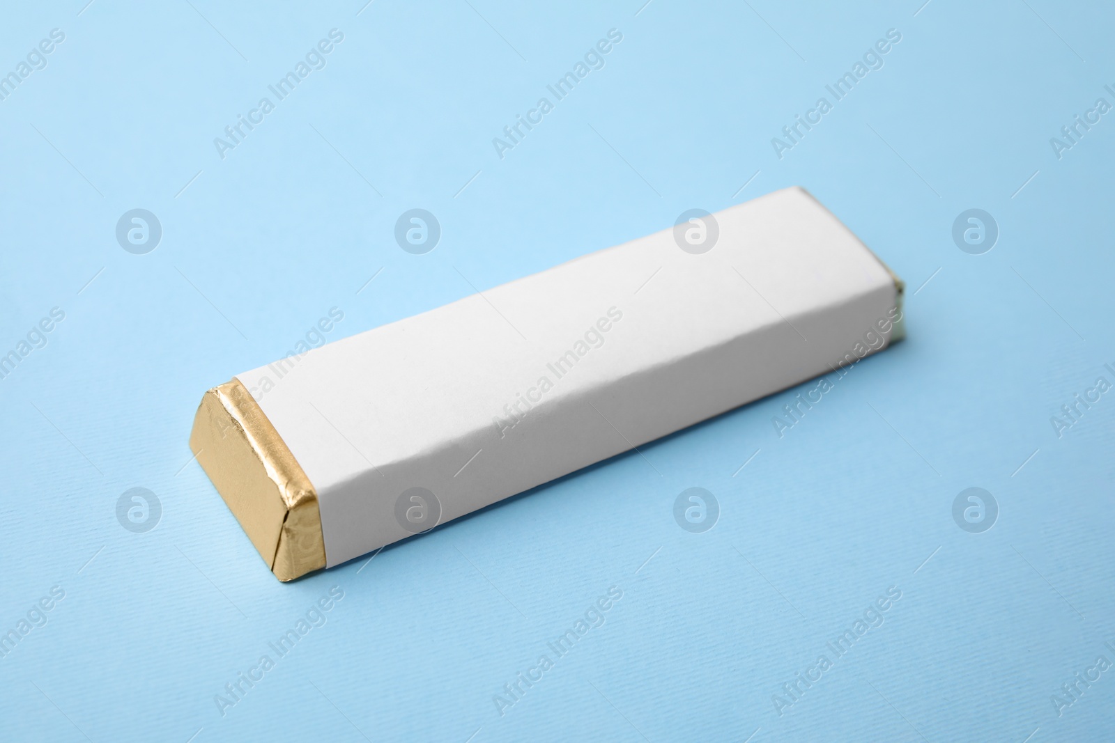 Photo of Tasty chocolate bar in package on light blue background