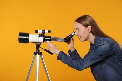 Young astronomer looking at stars through telescope on orange background