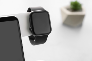 Photo of Stylish smart watch and phone charging with wireless pad against blurred background, closeup. Space for text