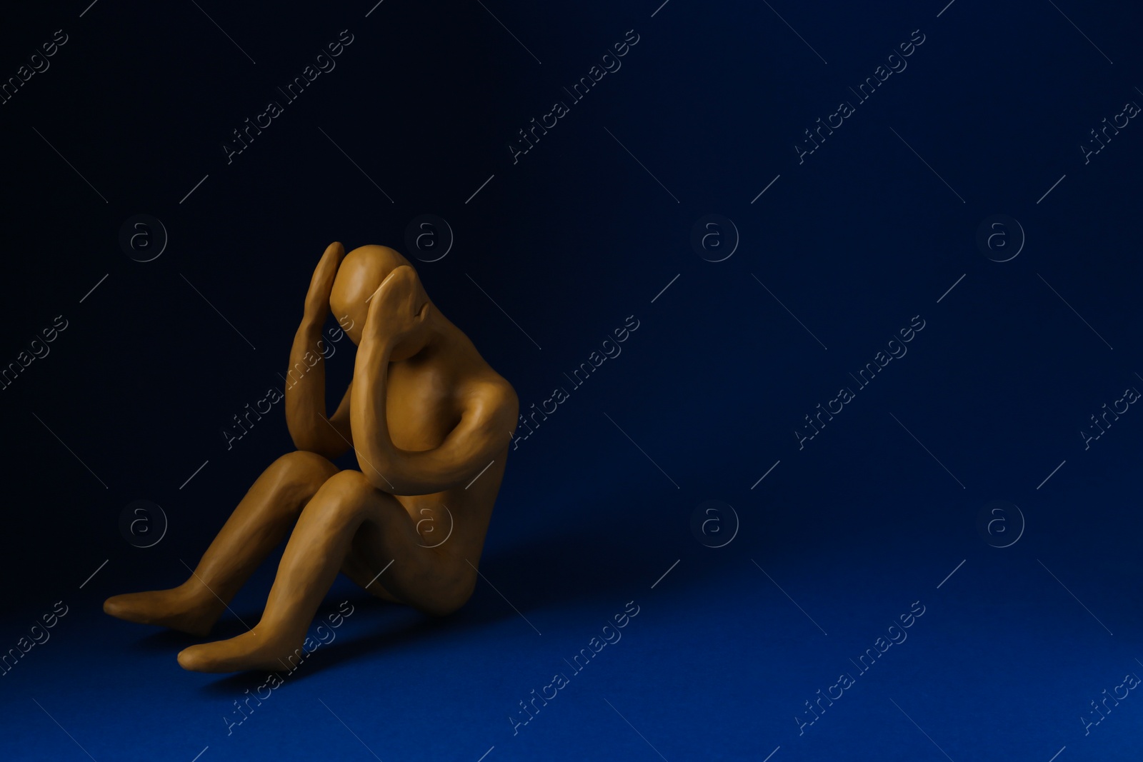 Photo of Plasticine figure of crying human on dark blue background. Space for text