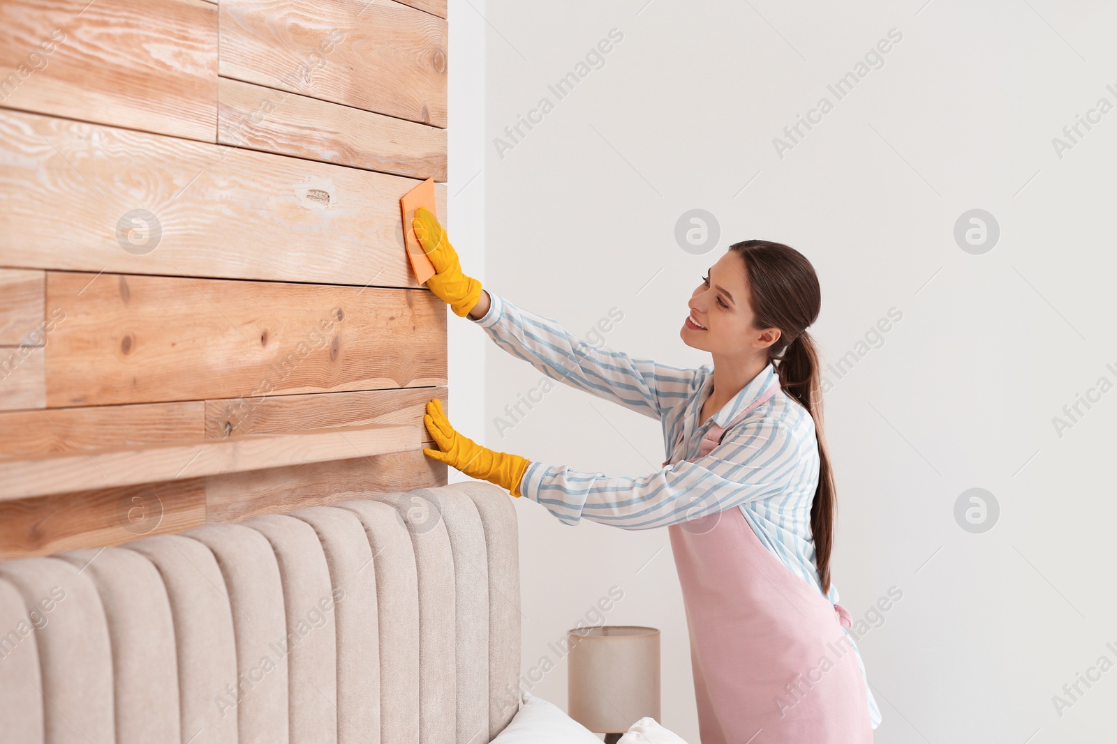 Photo of Young chambermaid wiping dust from furniture in hotel room