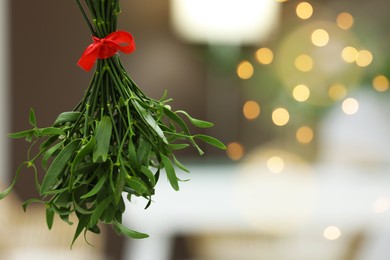 Photo of Mistletoe bunch with red bow on blurred background, space for text. Traditional Christmas decor