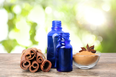 Bottles of essential oil, cinnamon sticks and powder on wooden table against blurred background