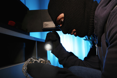 Thief taking jewelry out of steel safe indoors at night