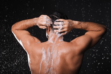 Photo of Man washing hair while taking shower on black background