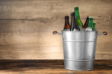 Photo of Metal bucket with beer and ice cubes on wooden table. Space for text