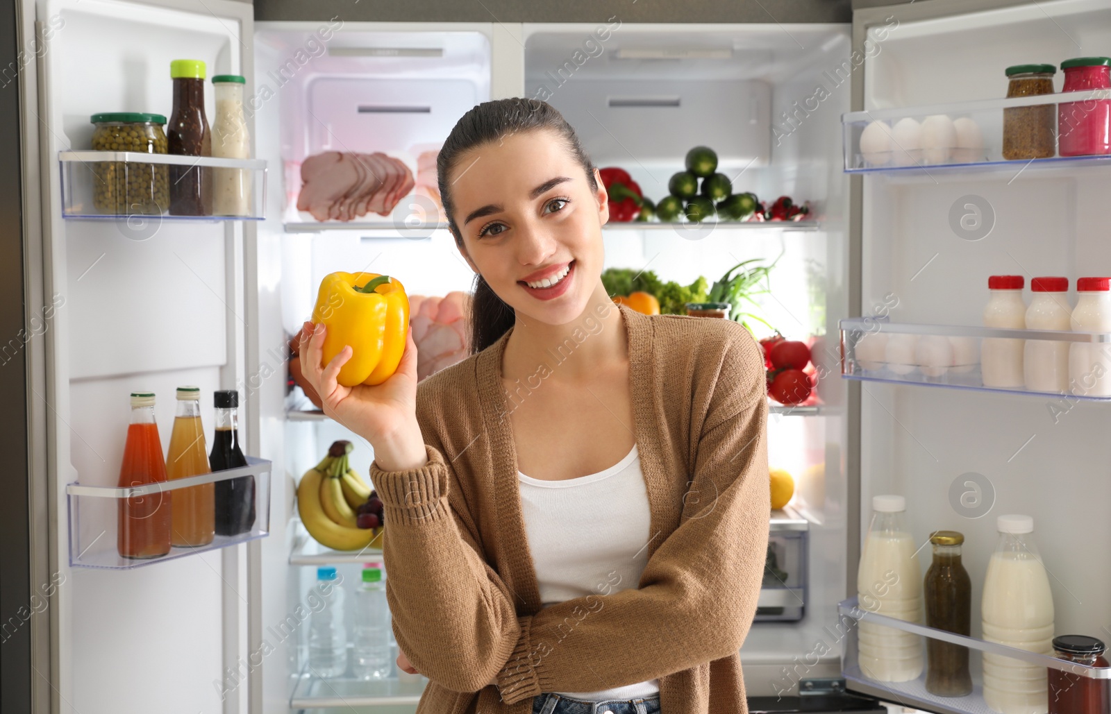 Photo of Young woman with bell pepper near open refrigerator