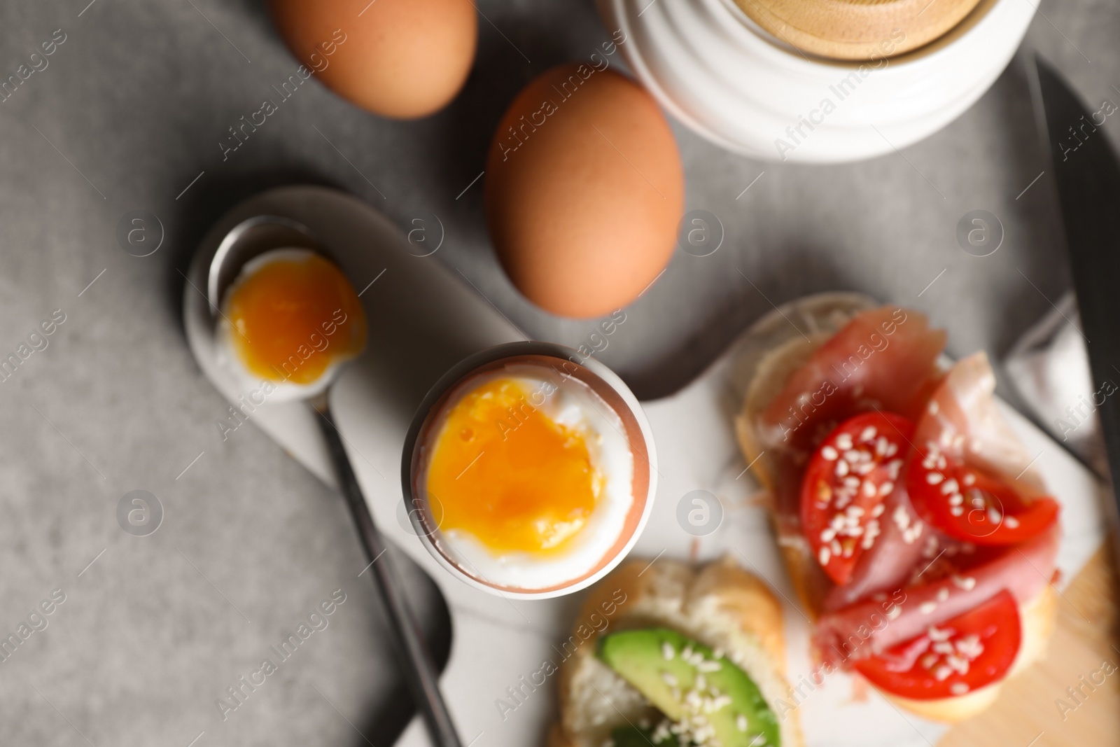 Photo of Fresh soft boiled egg in cup and sandwiches served on grey table, flat lay
