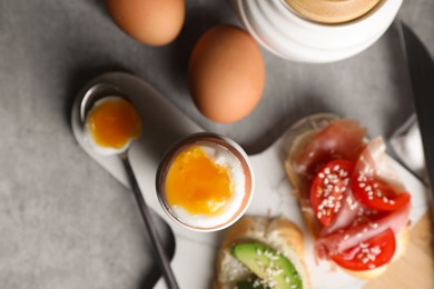 Fresh soft boiled egg in cup and sandwiches served on grey table, flat lay