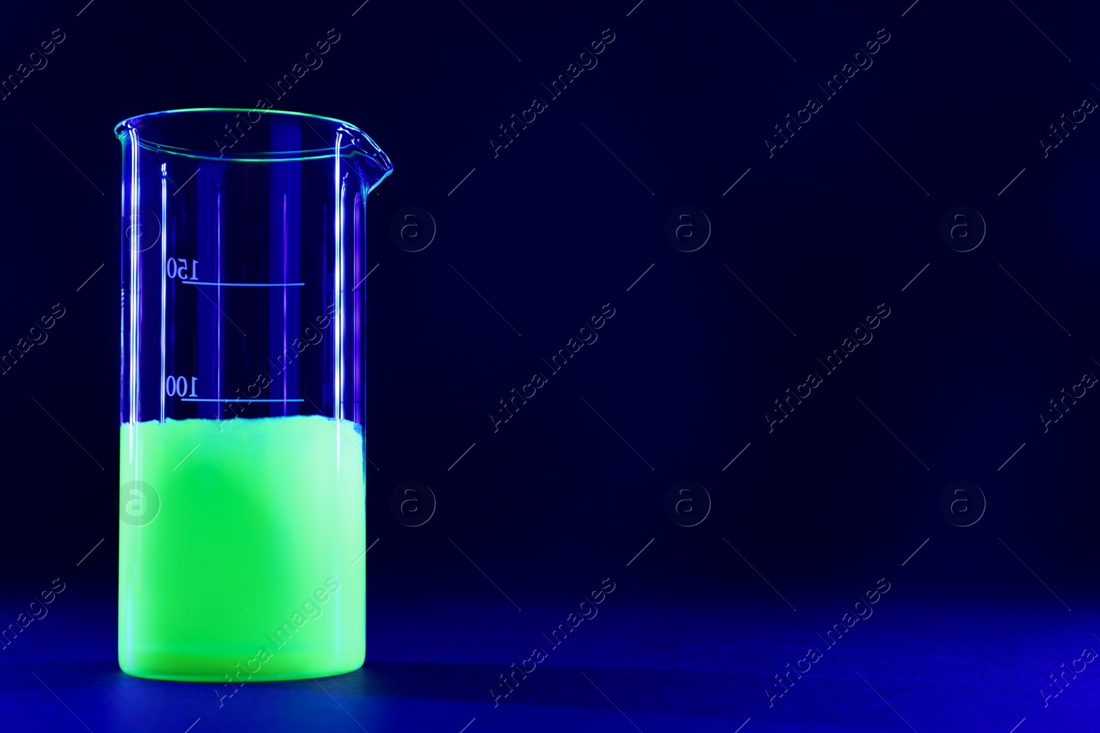 Photo of Laboratory beaker with luminous liquid on dark blue background, space for text