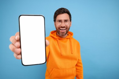 Handsome man showing smartphone in hand on light blue background