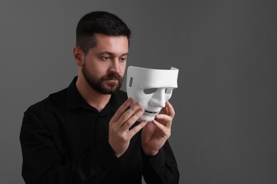 Photo of Multiple personality concept. Man putting on mask against grey background. Space for text