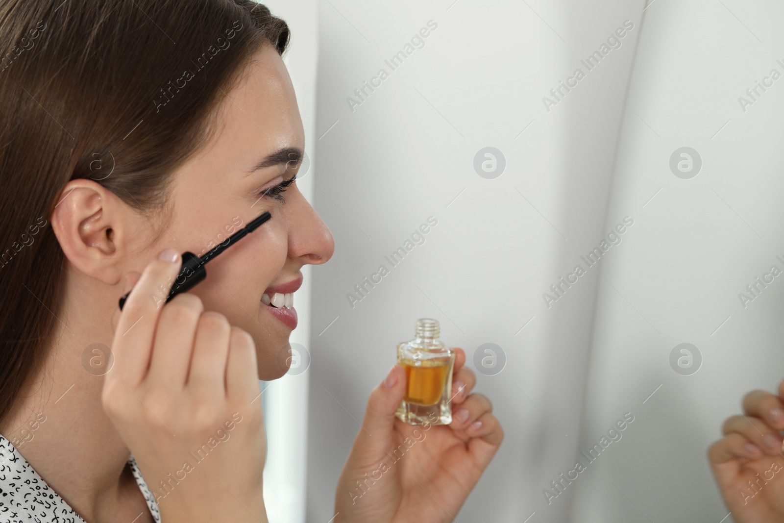 Photo of Young woman applying oil on her eyelashes indoors