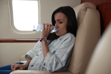 Nervous young woman with aviophobia drinking water in airplane