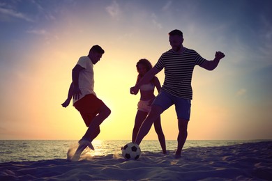 Friends playing football on beach at sunset