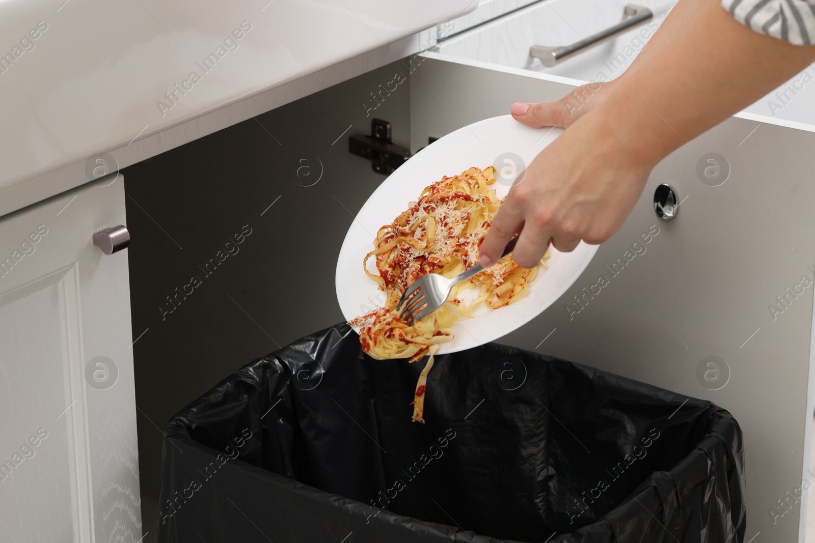 Photo of Woman throwing pasta into bin indoors, closeup