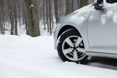 Car with winter tires on snowy road in forest, space for text