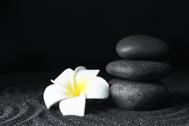 Spa stones and plumeria flower on black sand with beautiful pattern, space for text. Zen concept