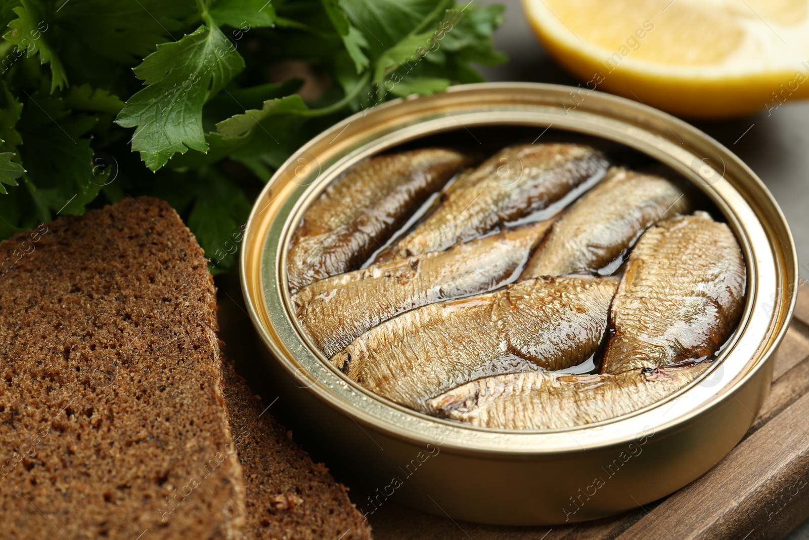 Photo of Tin can with tasty sprats served on wooden board, closeup