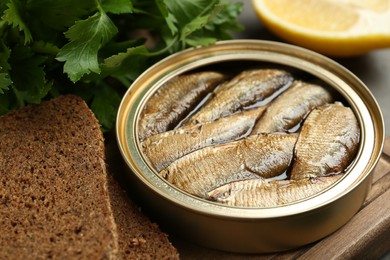 Tin can with tasty sprats served on wooden board, closeup