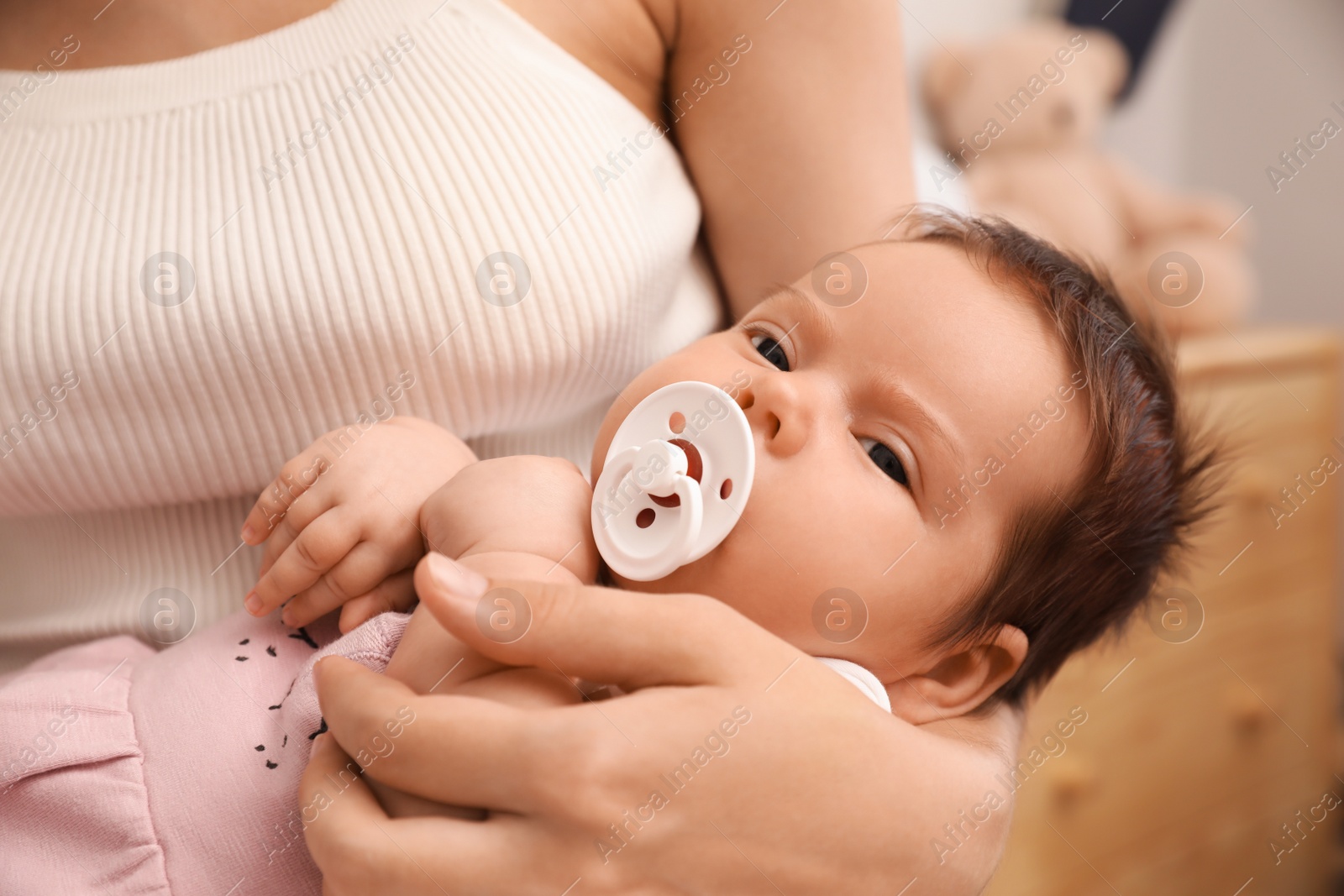 Photo of Mother holding her cute little baby with pacifier at home, closeup