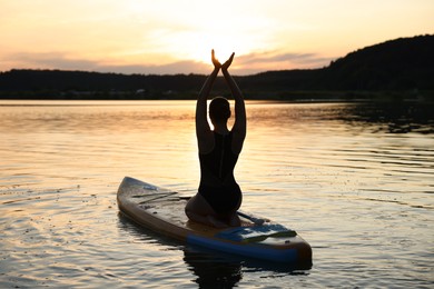 Woman practicing yoga on SUP board on river at sunset, back view