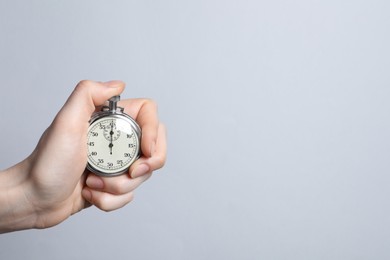 Photo of Woman holding vintage timer on light grey background, closeup. Space for text