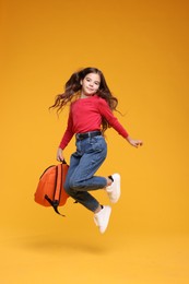 Photo of Back to school. Cute girl with backpack jumping on orange background