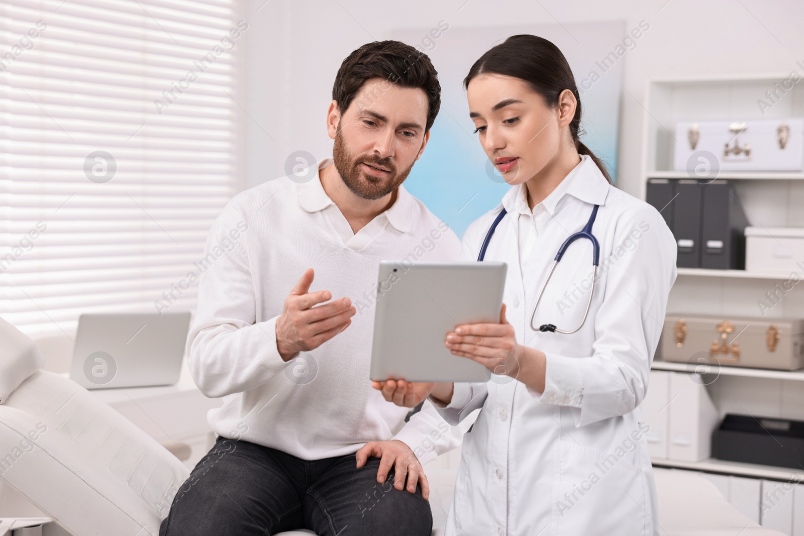 Photo of Doctor with tablet consulting patient during appointment in clinic