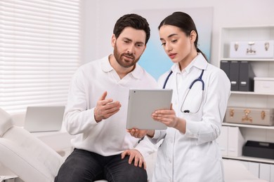 Doctor with tablet consulting patient during appointment in clinic