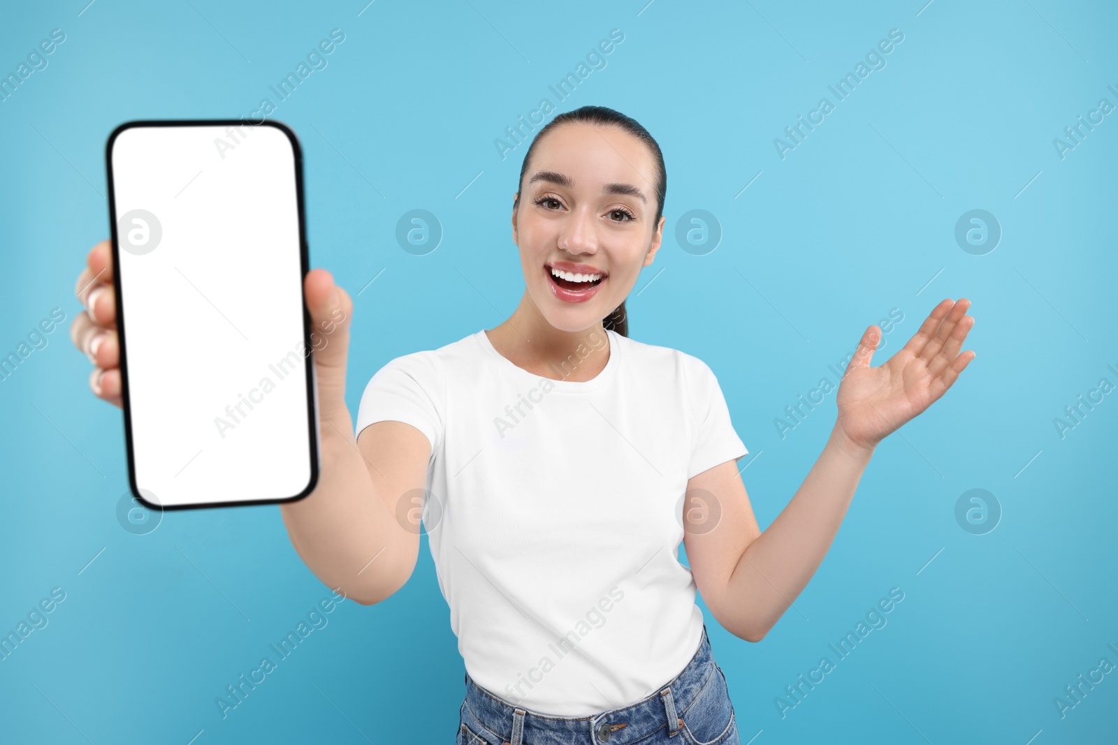 Photo of Surprised woman showing smartphone in hand on light blue background