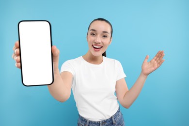 Surprised woman showing smartphone in hand on light blue background