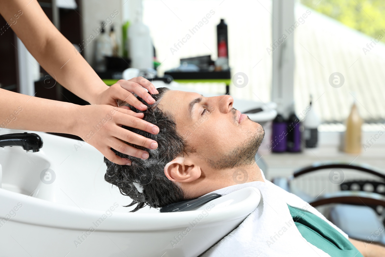 Photo of Stylist washing client's hair at sink in beauty salon