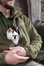 Soldier in uniform warming little stray cat indoors, closeup