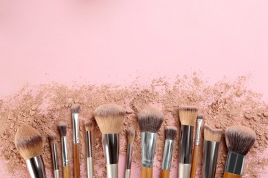 Photo of Makeup brushes and scattered face powder on pink background, flat  lay. Space for text