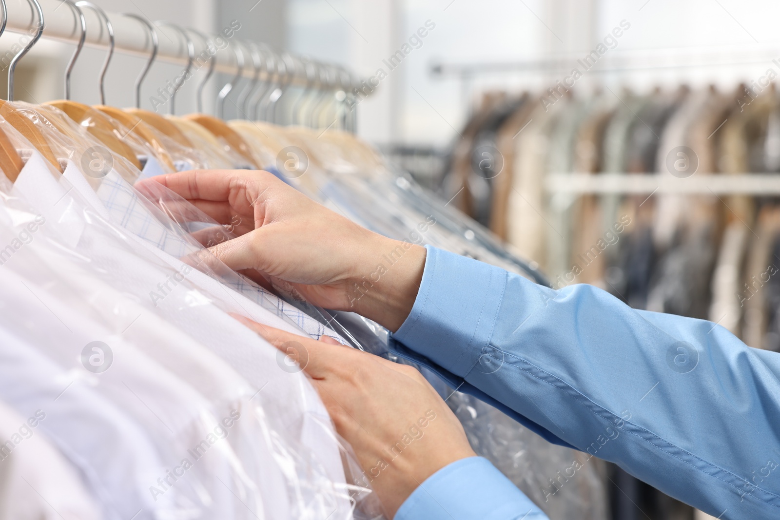 Photo of Dry-cleaning service. Woman taking shirt in plastic bag from rack indoors, closeup