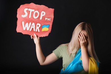 Photo of Sad woman hiding face and holding poster with words Stop the War on black background