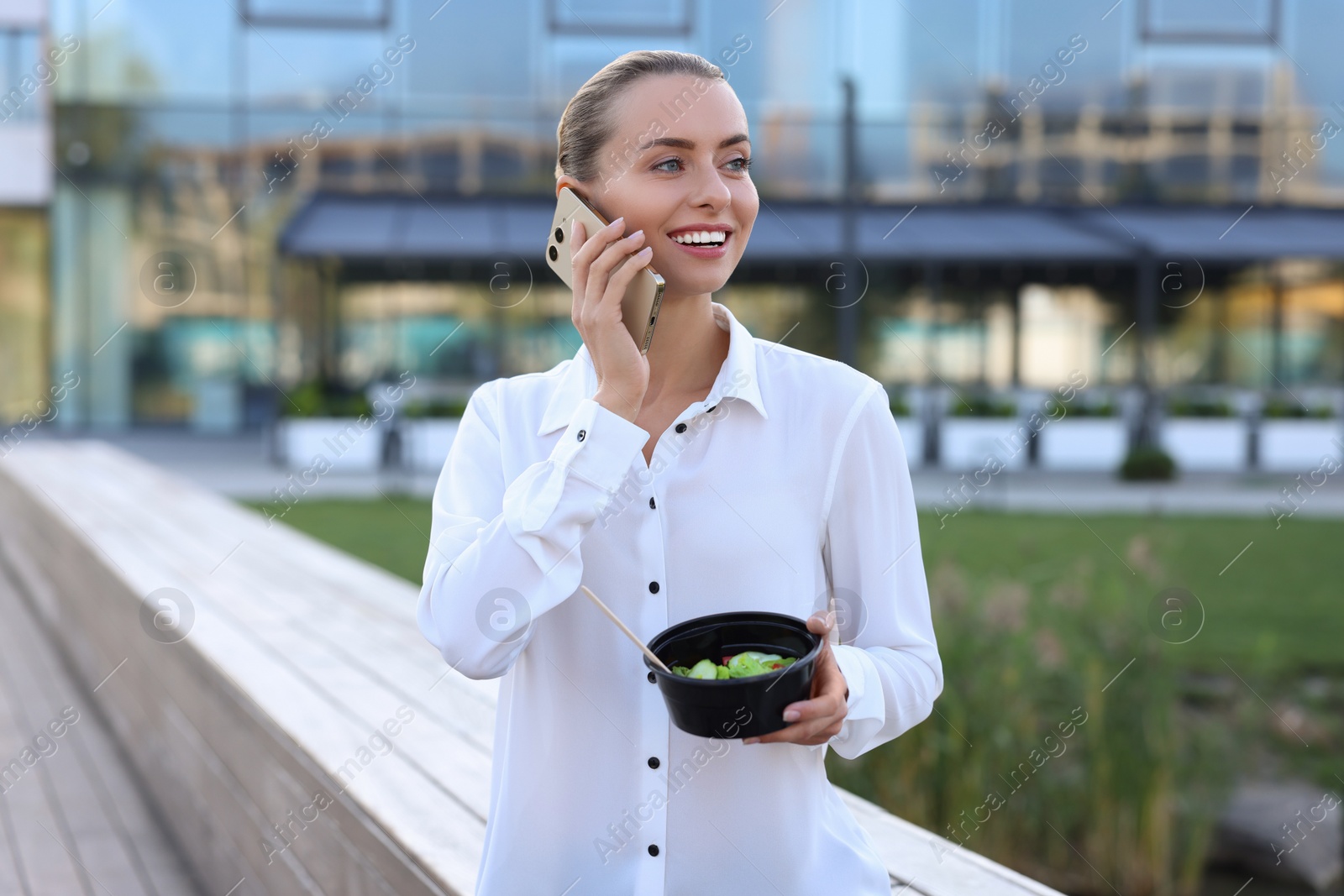 Photo of Smiling businesswoman talking on smartphone during lunch outdoors