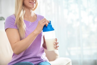 Photo of Young woman with bottle of protein shake at home, closeup. Space for text