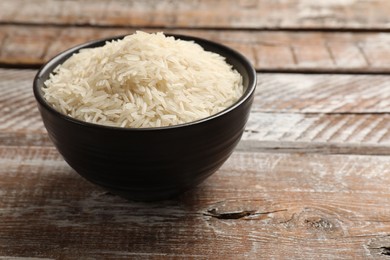 Photo of Raw basmati rice in bowl on wooden table, space for text